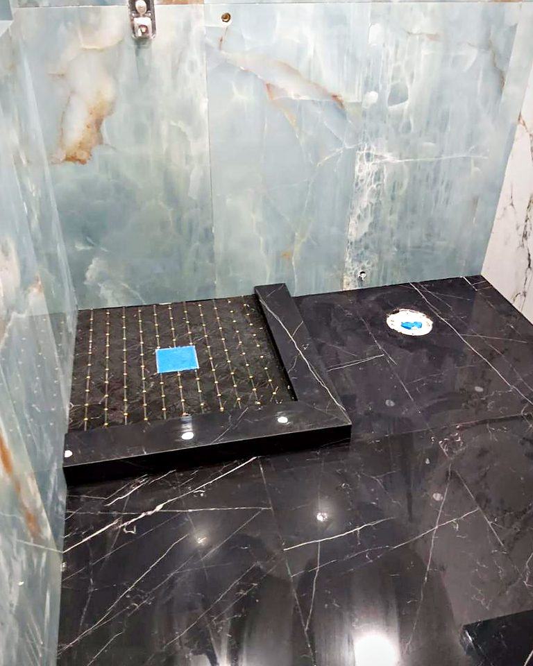 Custom shower with green onyx-look slab walls, black marble floor and a built-in bench