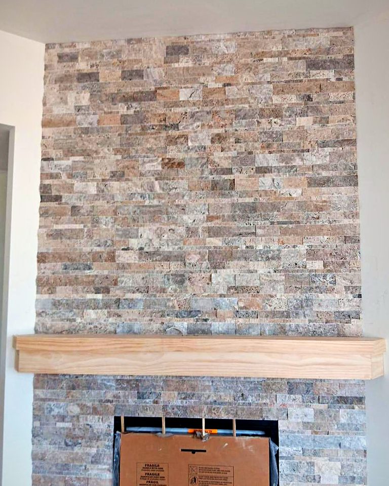 Split-face travertine fireplace wall with a raw oak mantel, firebox still covered